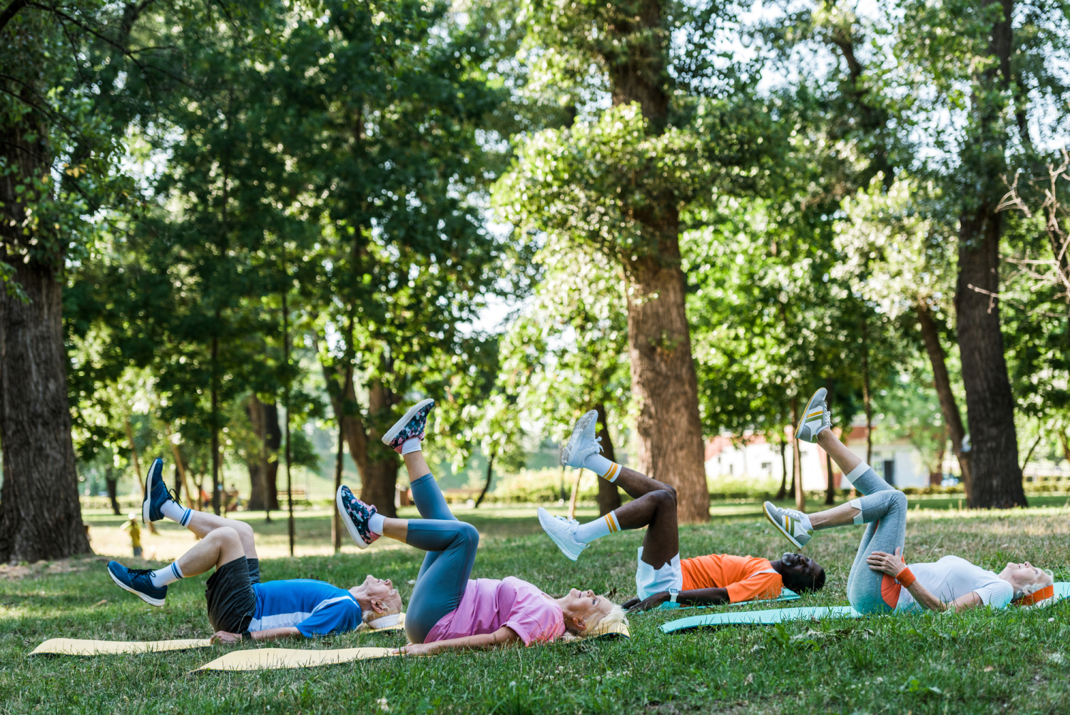 Personen liegen im Park auf dem Boden und führen leichte Beinübungen aus